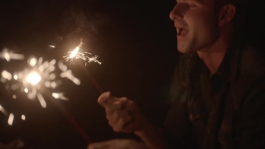 Man and woman holding sparklers outside at night