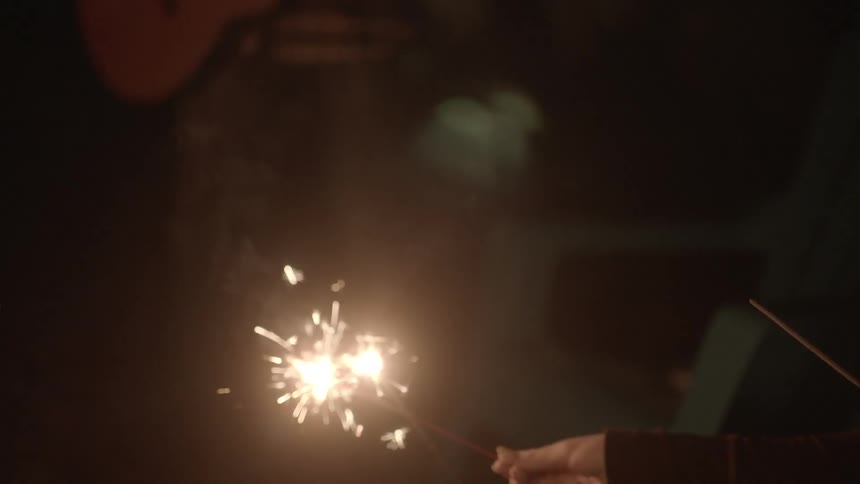 A sparkler is lit off a campfire by friends