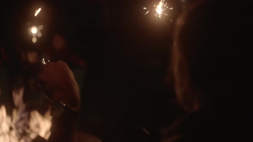 People sit around a campfire holding sparklers