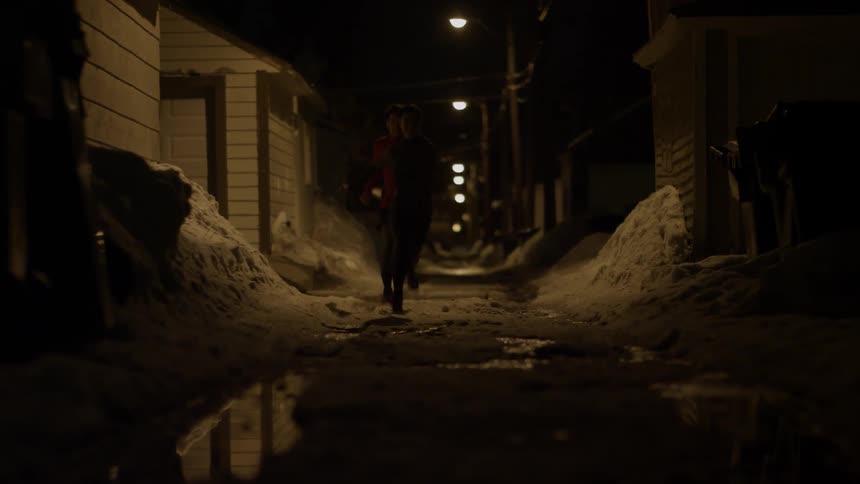 Man and woman run outside in a snowy alley at night