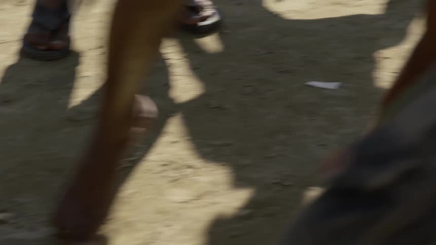 Barefoot children play soccer on dirt