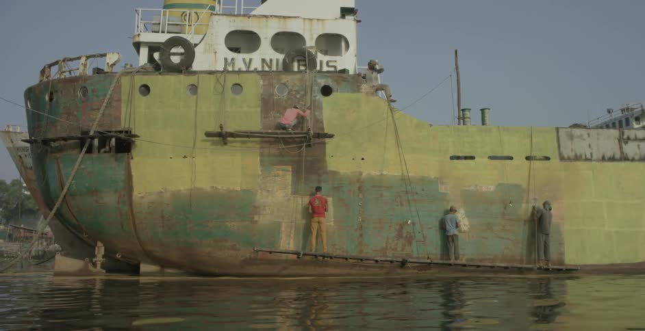 Several men paint a large rusty ship
