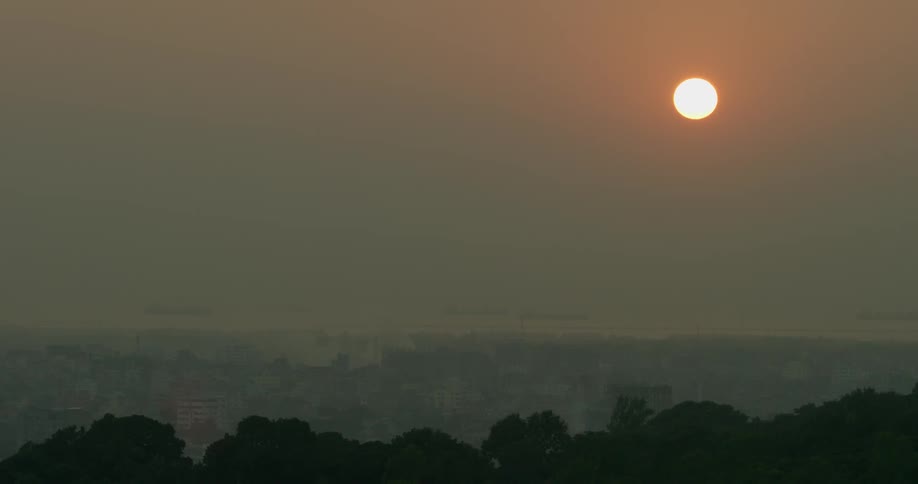 The sun shines through the haze overtop of a city