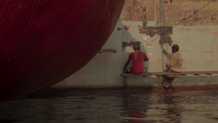 Two people sit above a canal of water pounding on a wall