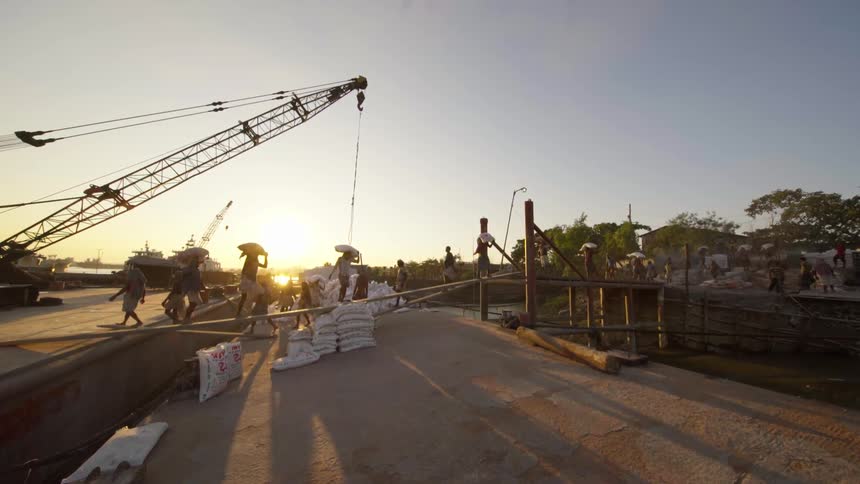 People carrying heavy white bags over a small wooden bridge