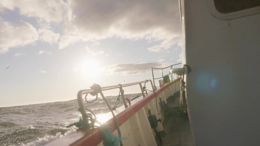 A ship floats on the open sea as the sun shines down
