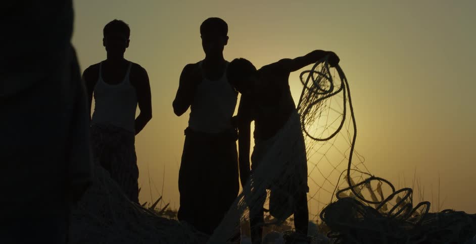 Three men stand outside as one man picks up some netting