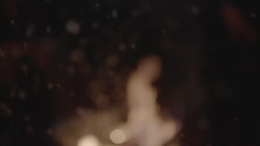 People sit around a campfire outdoors as embers float through the air