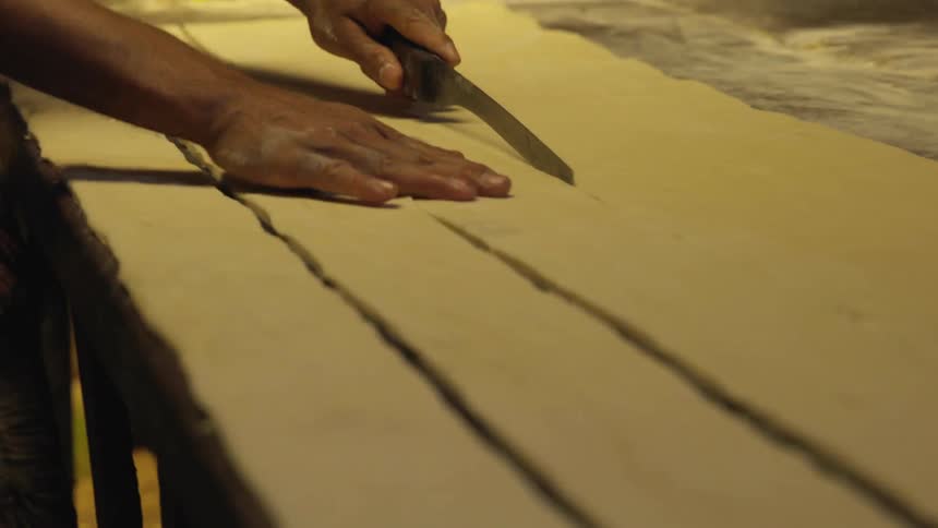 A person uses a knife to cut dough into long strips