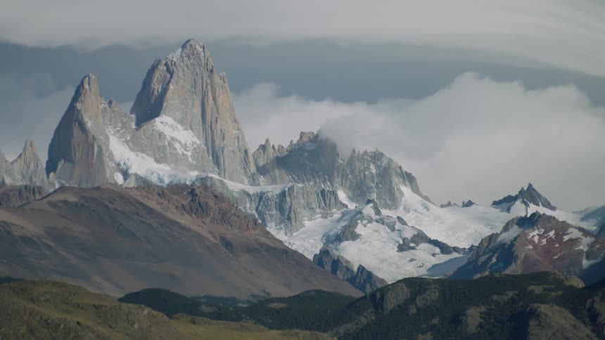Clouds hang above and in between snowy mountains