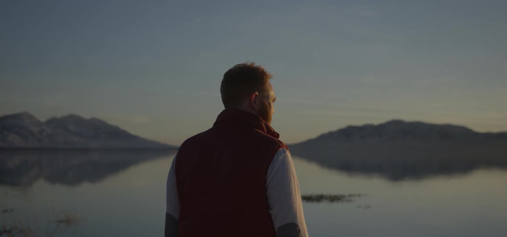 A man is standing near a lake at sunset