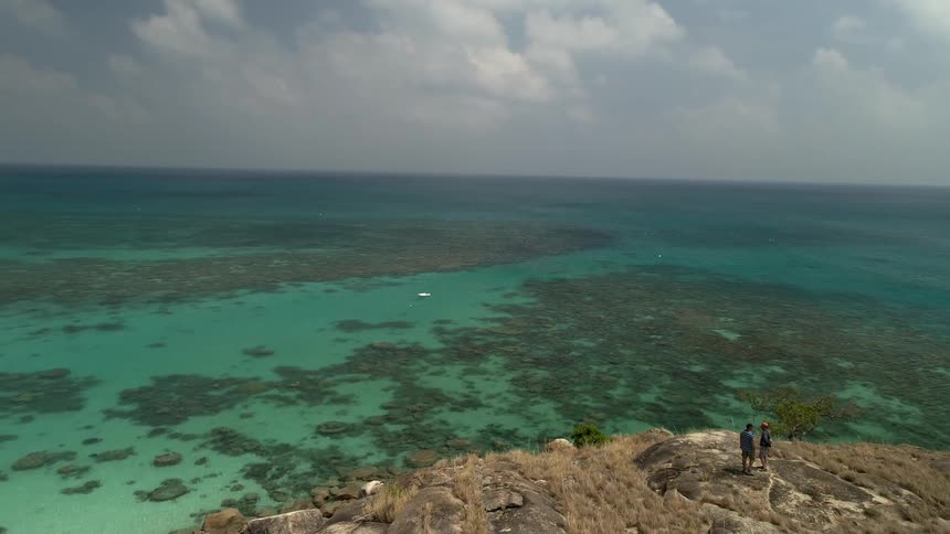Two people are standing on a point overlooking the crystal clear blue green sea