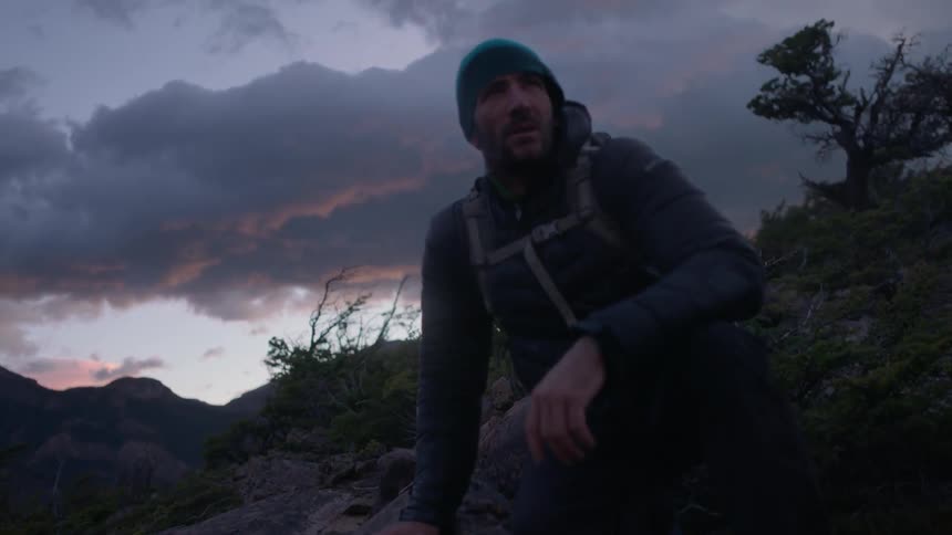 A man crouches on the rocks on the hill on a windy day