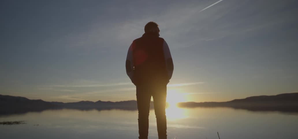 A man stands overlooking a lake at sunset