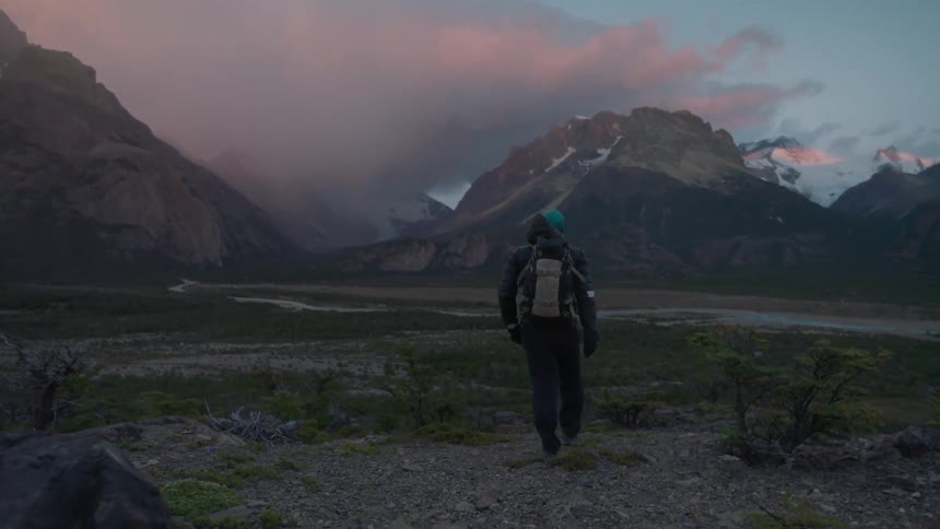 A man hikes near mountains on a windy day