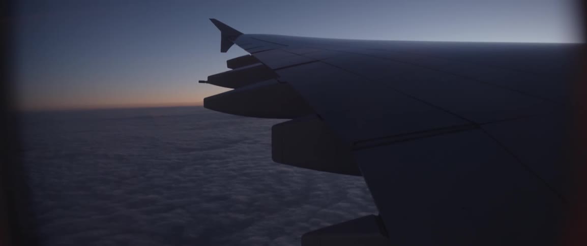 Clouds below an airplane wing and sunset on the horizon