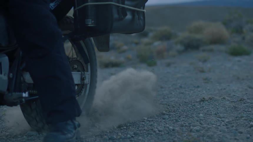A motorbike begins to move and stirs up some dust