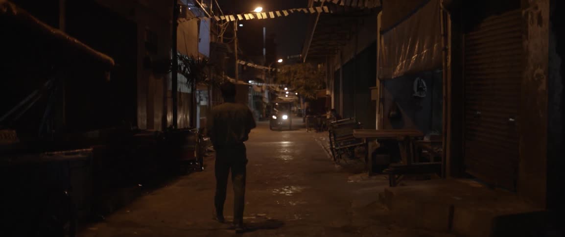 A man walks down an alley while a car approaches at night