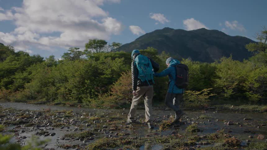 A man and woman hold hands as they hike across a stream bed