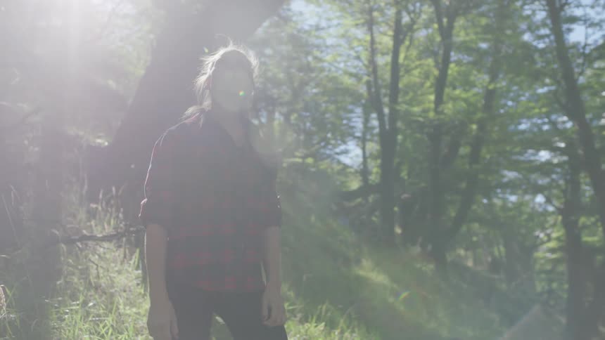 A woman stands in a forest on a sunny day