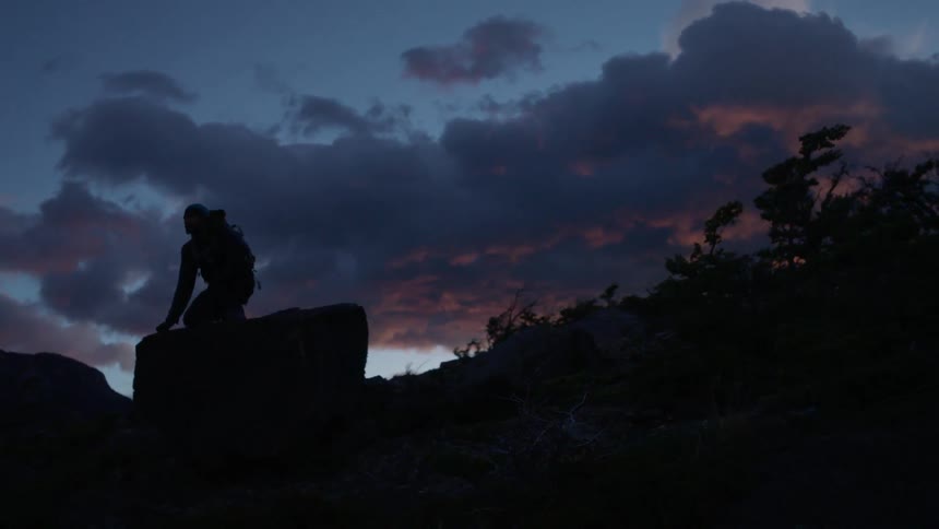 A person is kneeling down on a rock at sunset