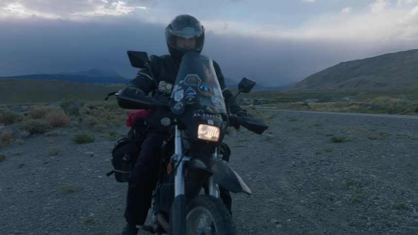 Man riding off on motorcycle on mountain highway during cloudy day