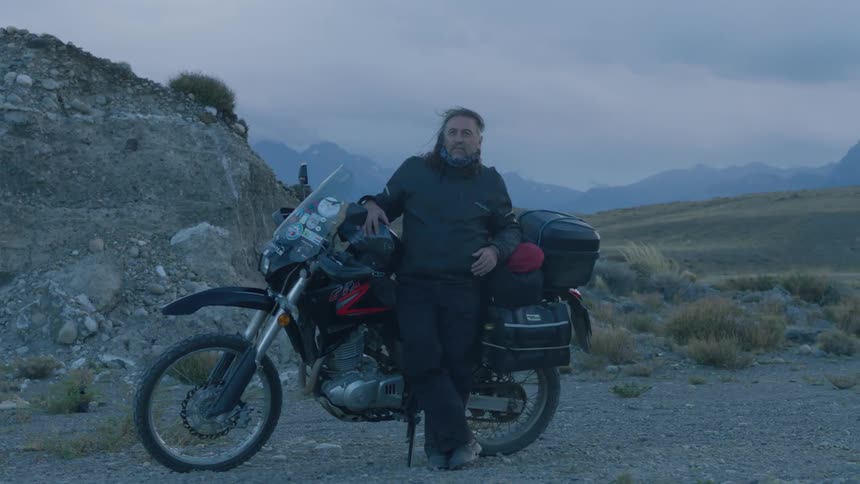 A man is leaning against his motorcycle in the desert