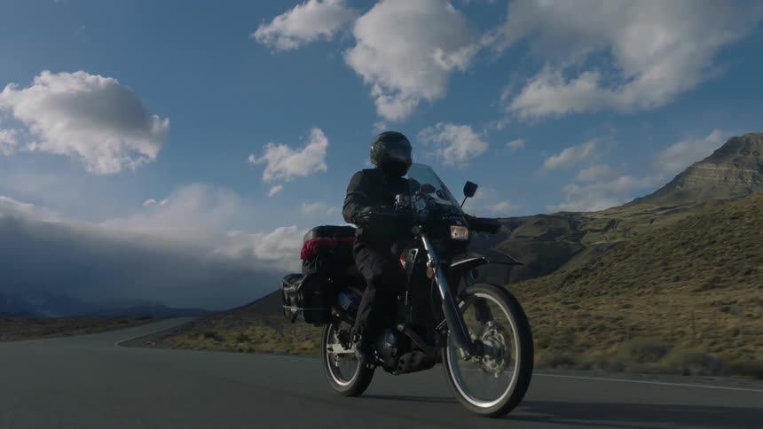 Person riding motorcycle on mountain highway on cloudy day