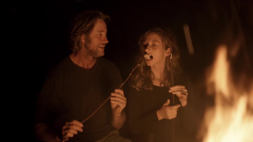 A man and girl eat marshmallows roasted on a fire