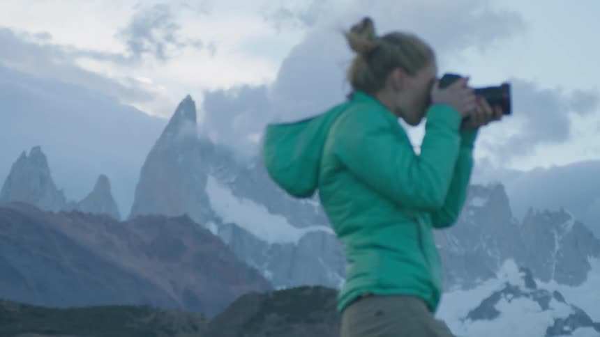 A woman takes a photograph in snowy mountains