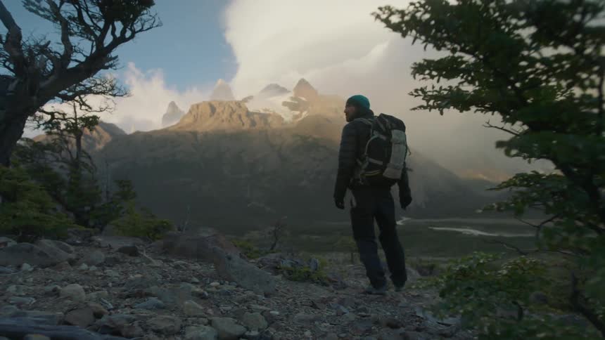 Man wearing backpack walking in mountain wilderness on windy day
