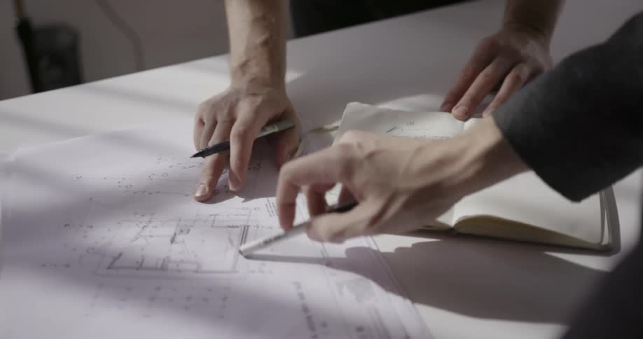 Two men look at blueprints on a table