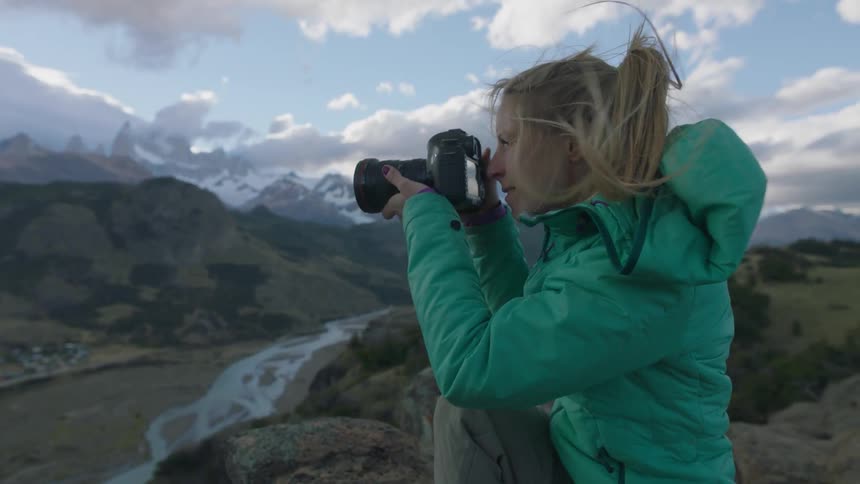 A woman is sitting on the edge of a mountain taking pictures