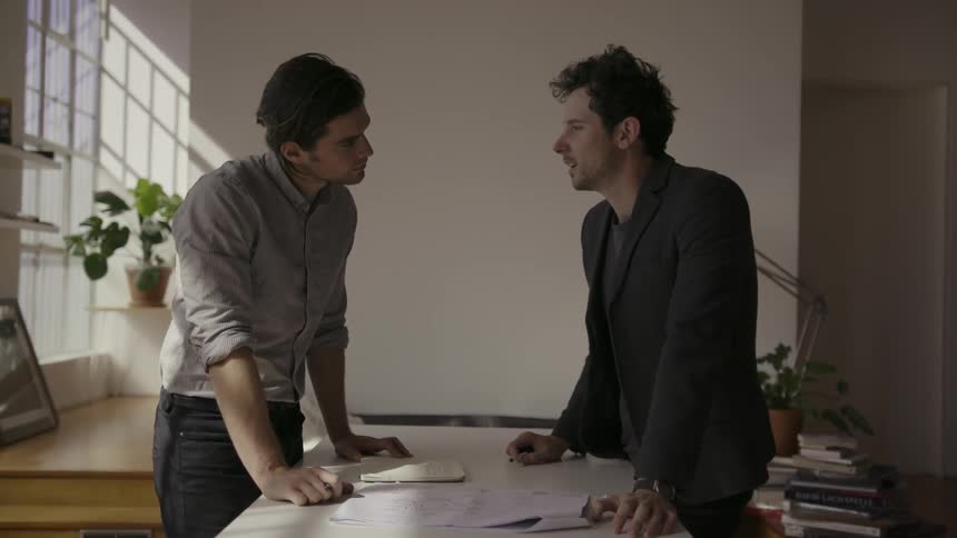 Two men are having a discussion and looking at papers on a table