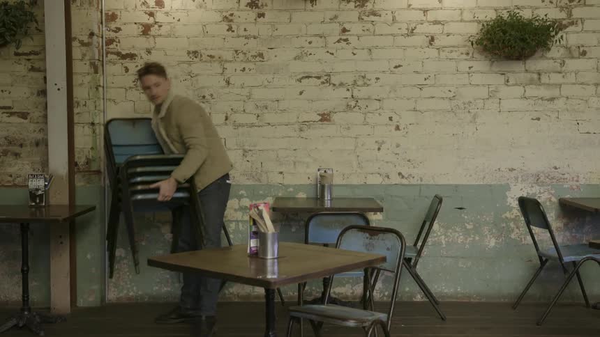 A man lifts some chairs up and walks off