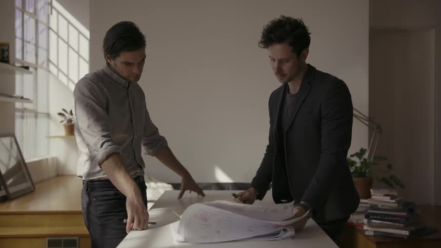 Two men talk while looking at various papers on a desk