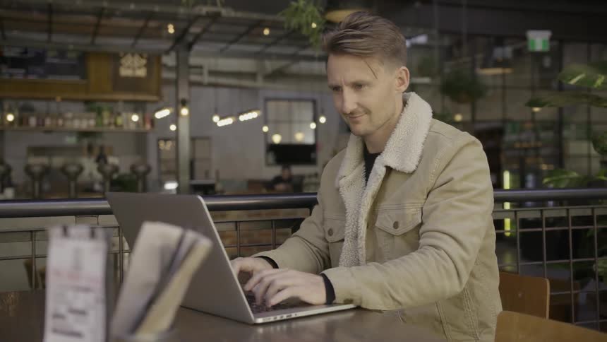 A man is in a restaurant typing on his laptop