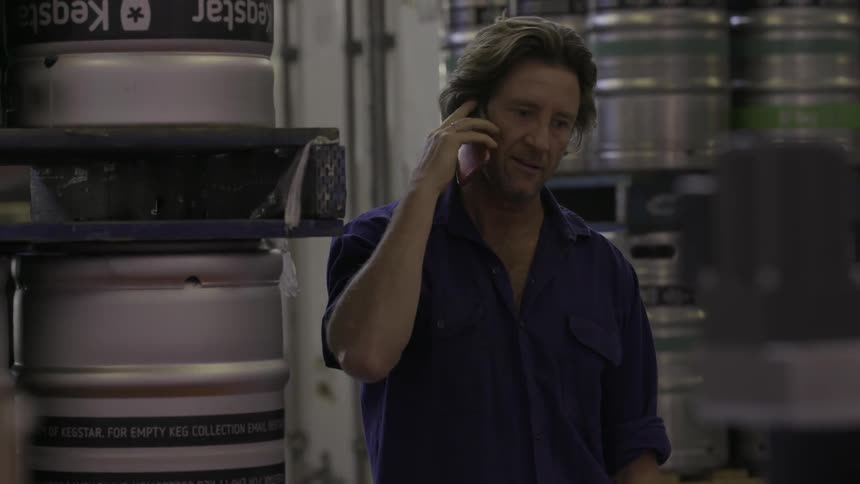 A man talks on a phone while standing near stacked metal barrels