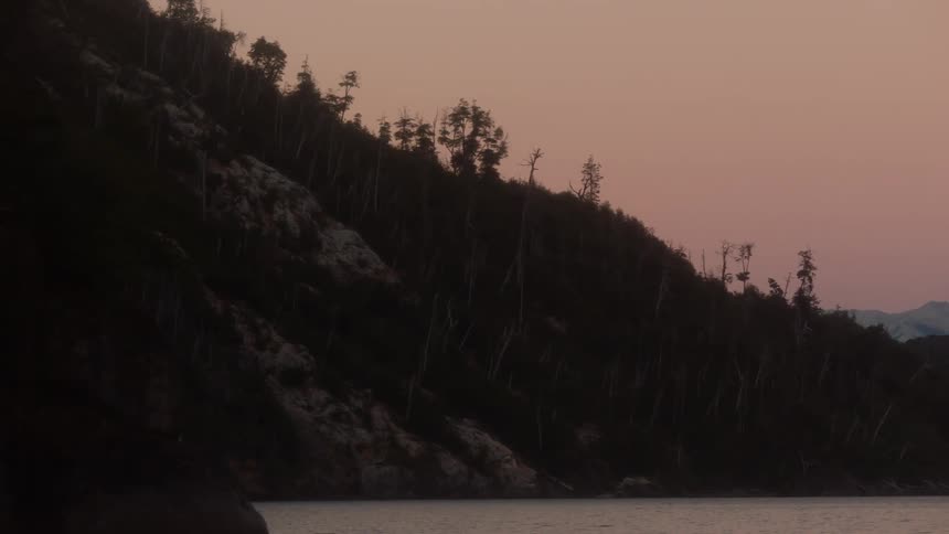 A tree covered hillside wraps around a lake at sunset