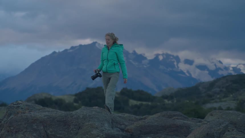 A woman carrying a camera steps onto a rock to take a picture