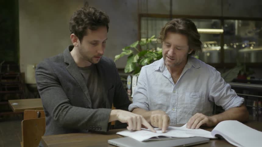 Two men talk while pointing at a sheet of paper