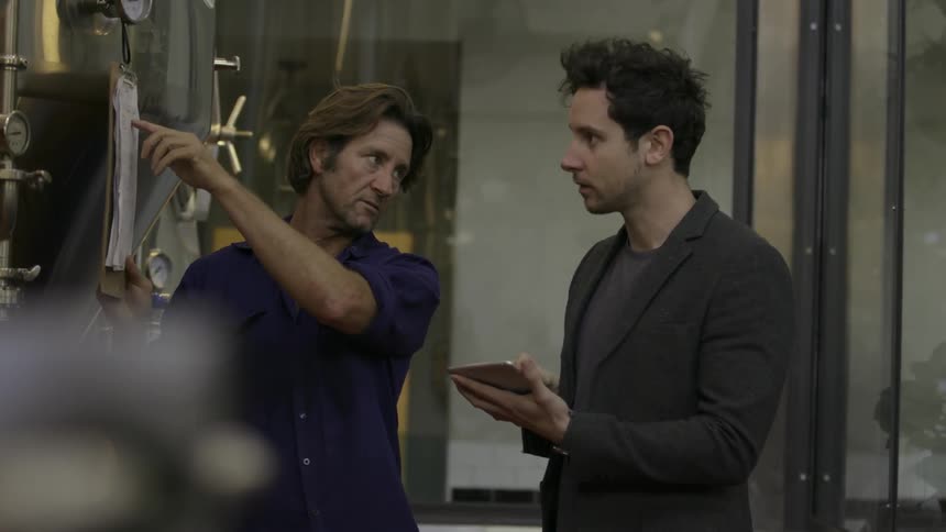Two men discuss something written on a hanging clipboard