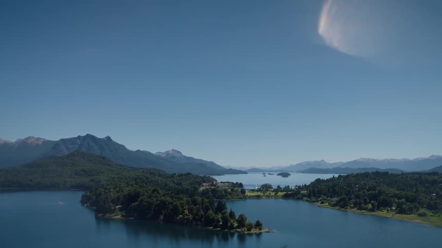 A large lake is surrounded by green hills and steep mountains