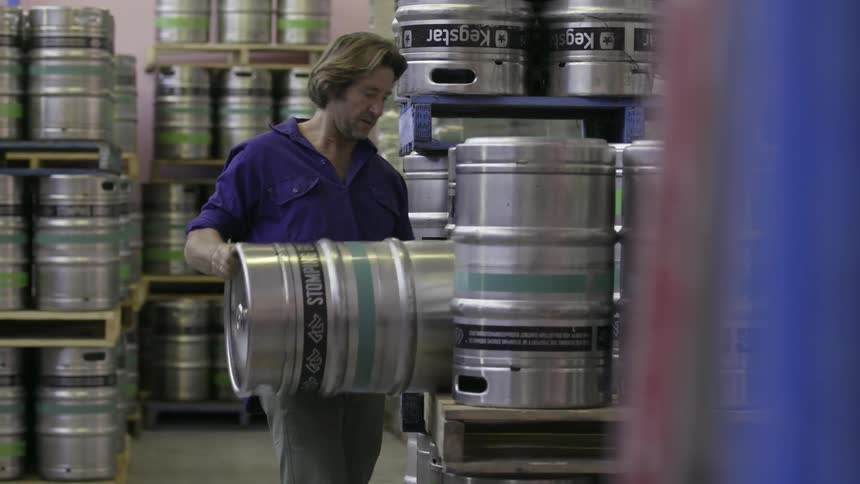 Man puts a keg on a shelf next to many kegs