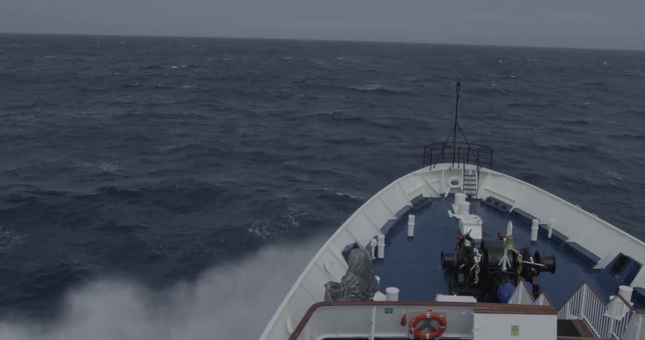 Moody Ocean waves crash over the bow of a boat at sea