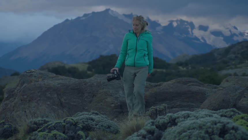 Woman carrying a camera walks over hilly landscape