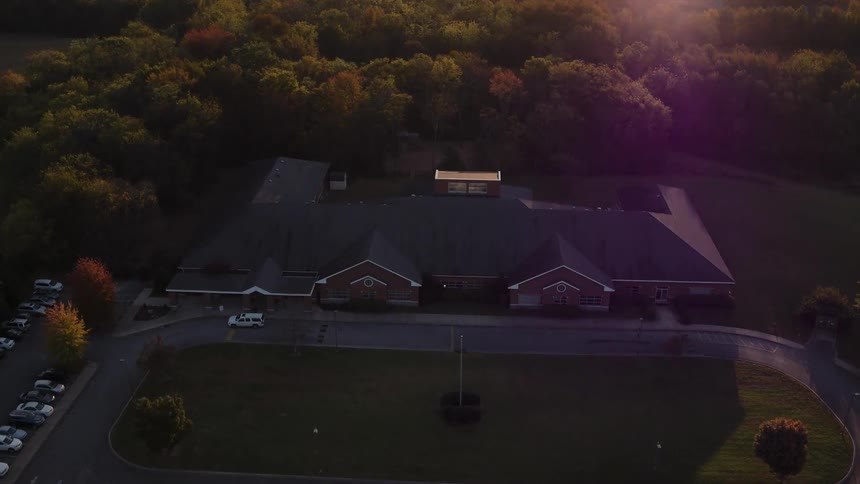 A large building is shown surrounded by fall trees at sunset