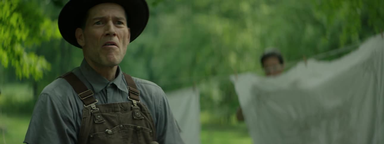 A man digs in a lawn while a woman hangs laundry on a clothesline