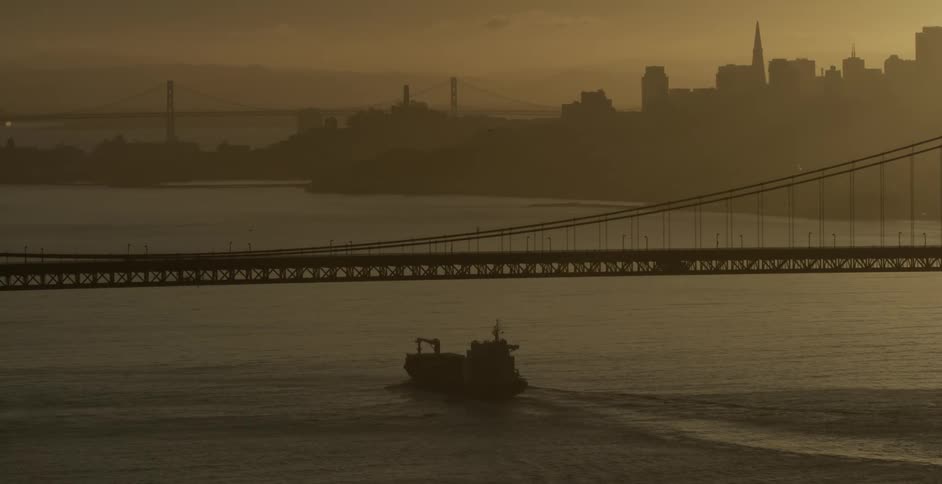 A ship passes under a suspension bridge at sunset