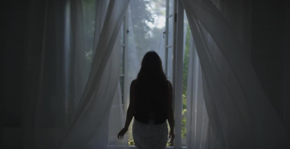 A woman opens up the curtains and window